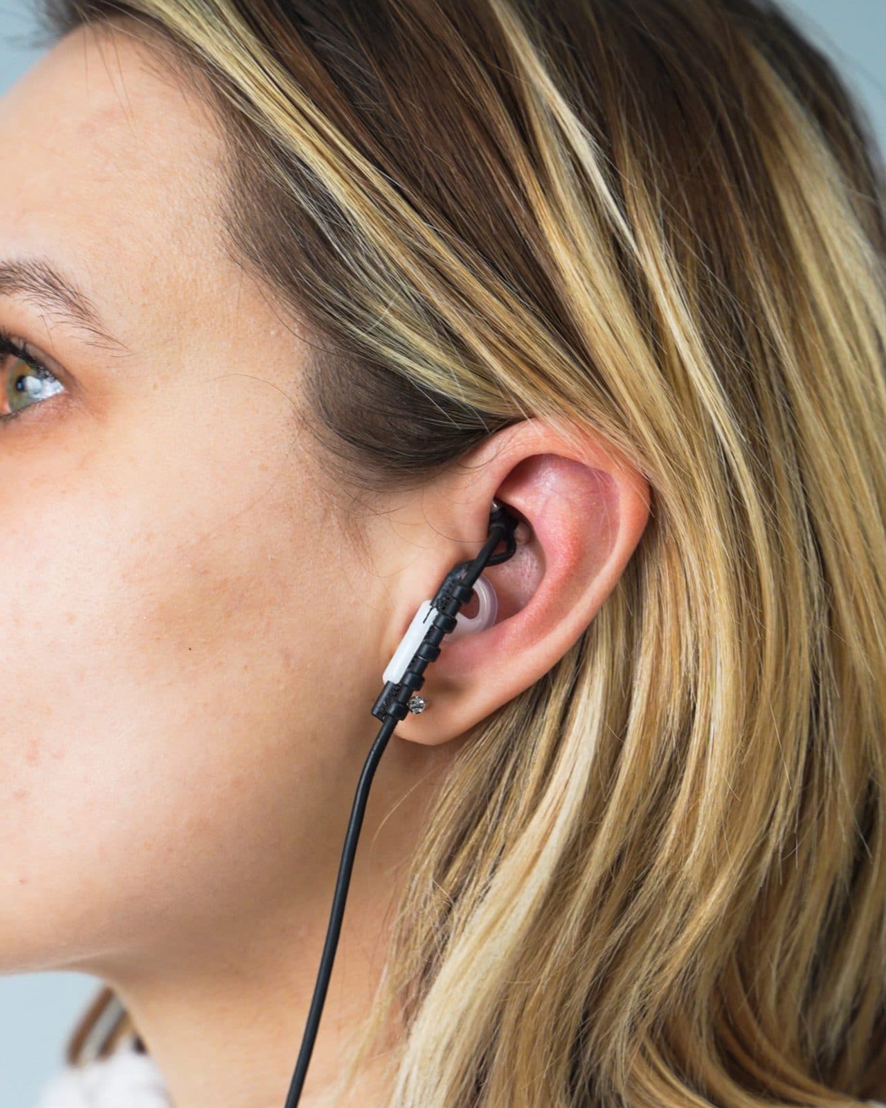 Close-up of the tVNS ear electrode worn in the outer ear, its thin cable running down from the ear